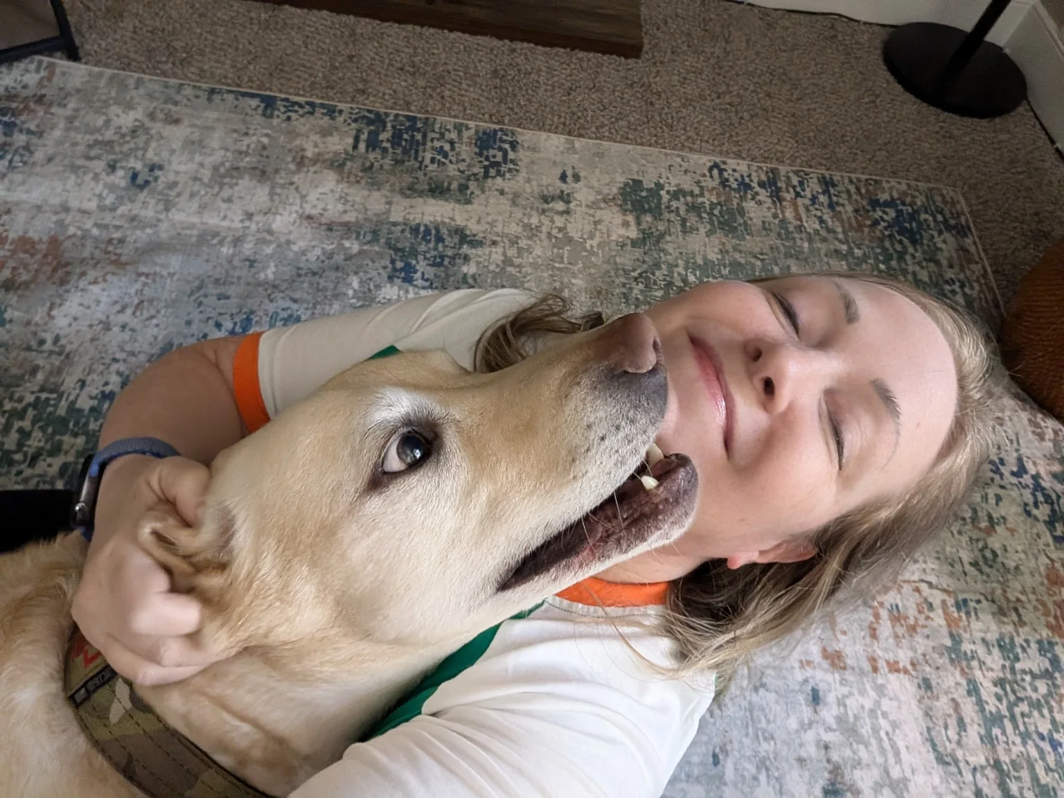 Kendall relaxing on a rug with Landon, her yellow Labrador service dog, looking up affectionately at her